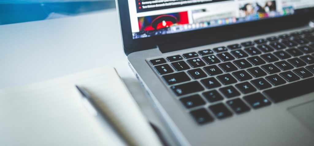 Aktualności, zdjęcie przedstawiające fragment laptopa oraz notatnika leżące na stole